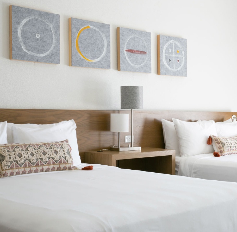 A hotel room with two beds, wooden headboards, and artwork on the wall.