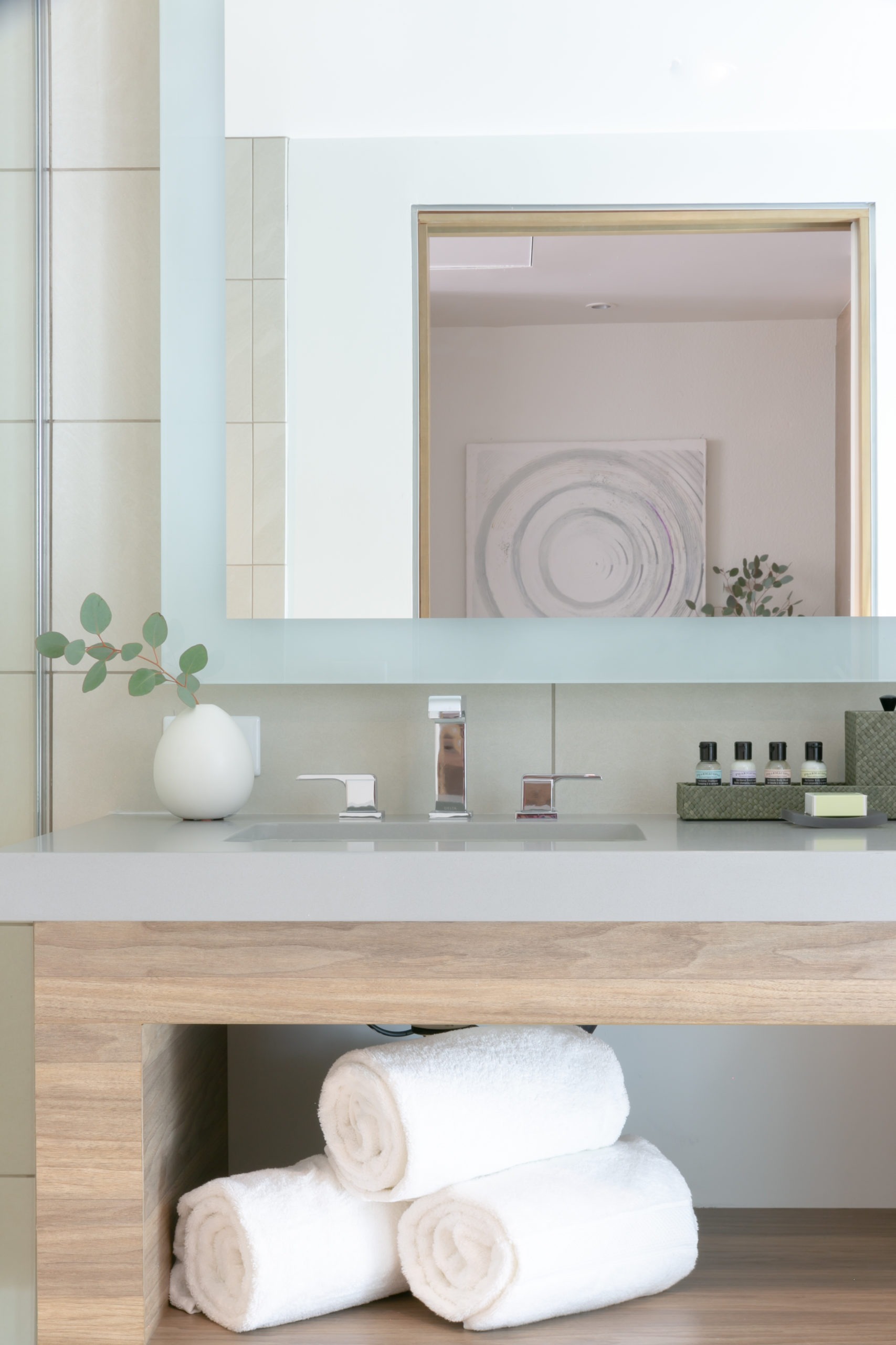 A clean bathroom sink area with a large mirror, towels, and toiletries.