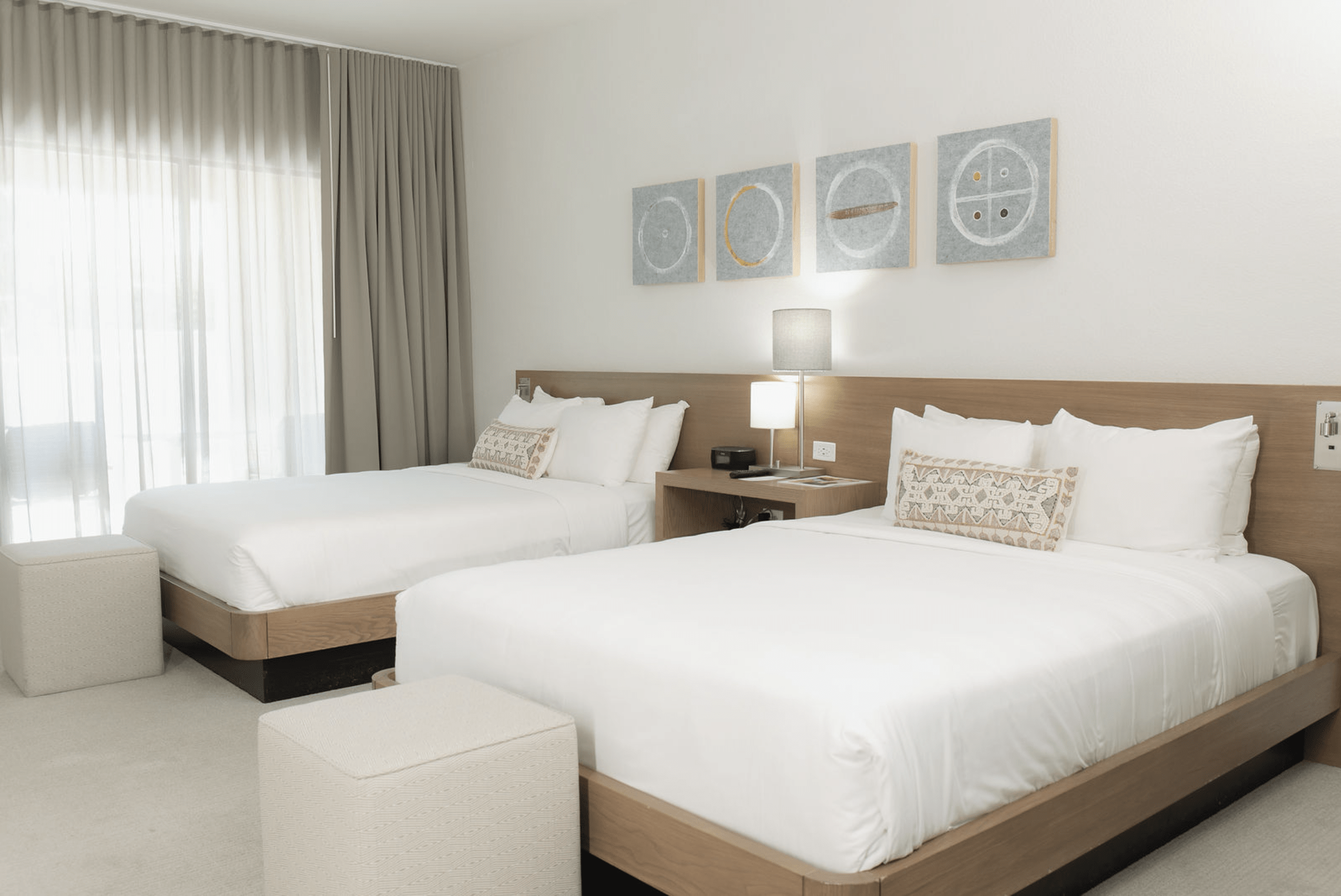 A hotel room with two queen beds, wood headboards, white bedding, and artwork above the beds.