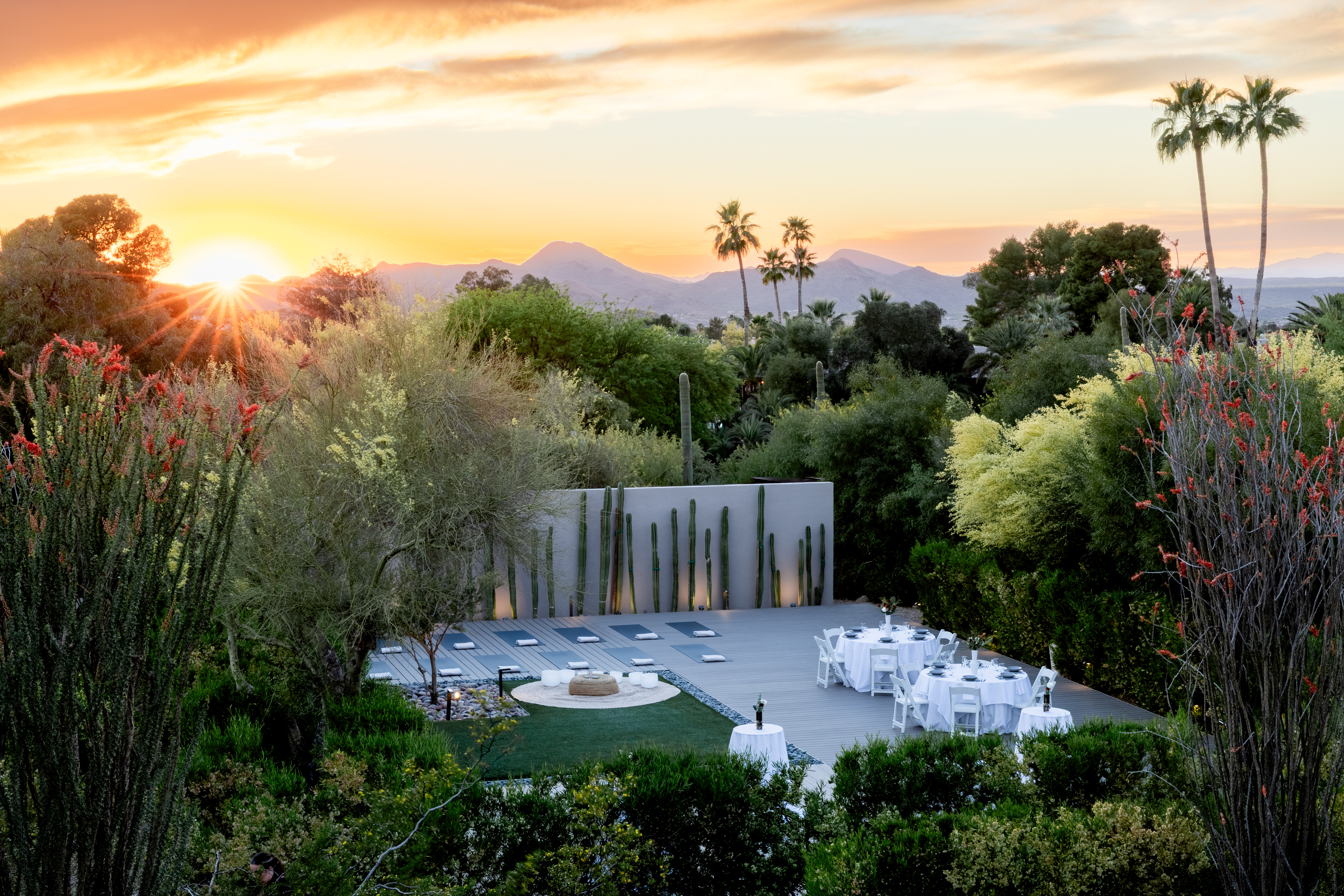 A scenic outdoor space with a fire pit, tables and chairs, and a mountain view at sunset.