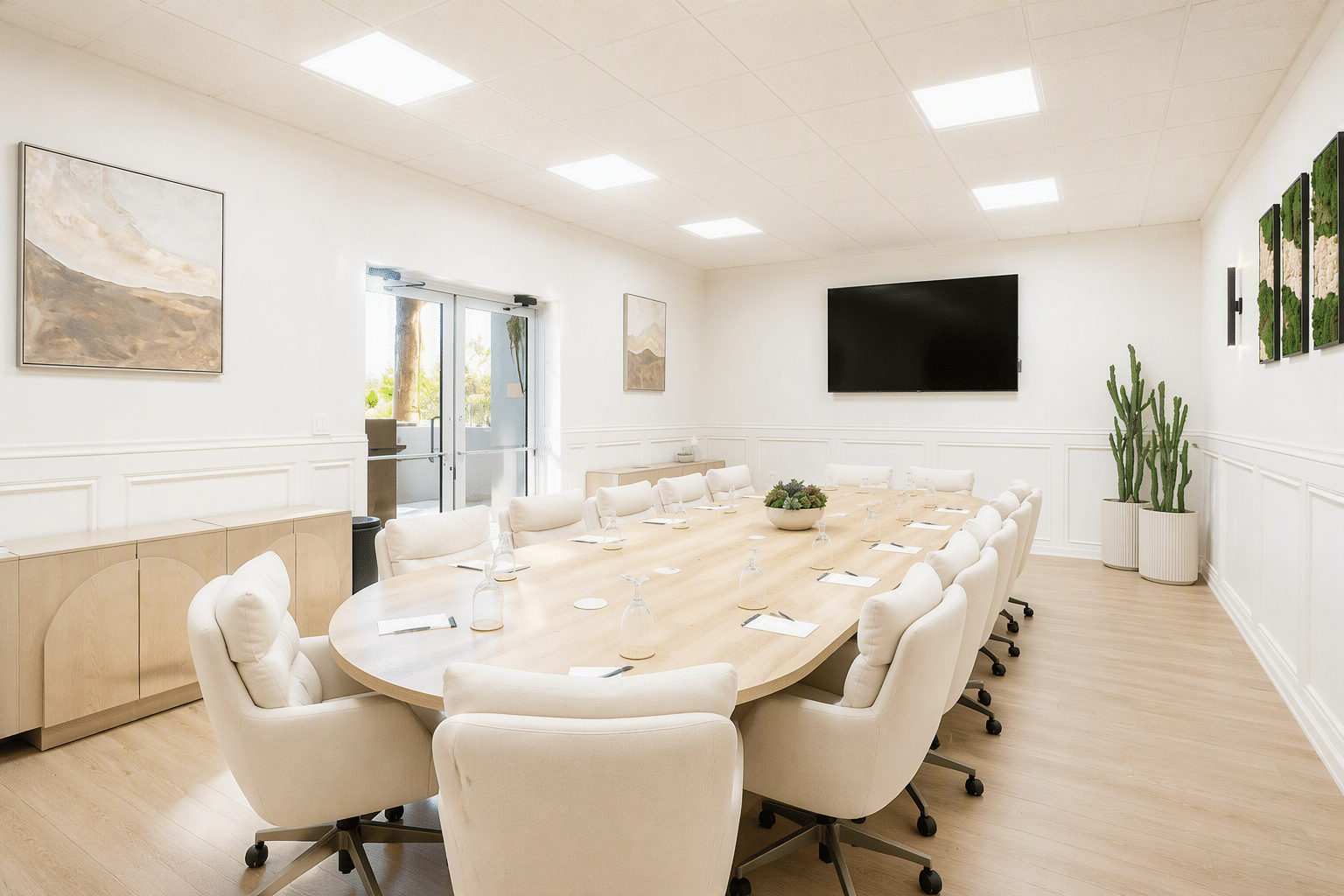 A well-lit meeting room with a large round table, white chairs, and a large screen on the wall.
